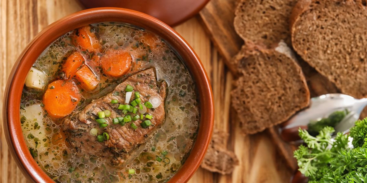 Bowl of roast and carrots in an orange crock next to dark wheat bread on a wooden cutting board