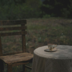 wooden chair and a round table with white linen sitting in an open field