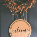 a wreath and round wooden sigh that says "welcome" hanging on a black door