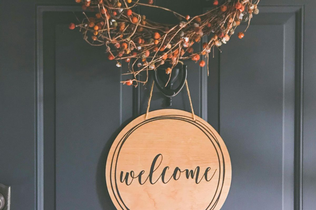 a wreath and round wooden sigh that says "welcome" hanging on a black door