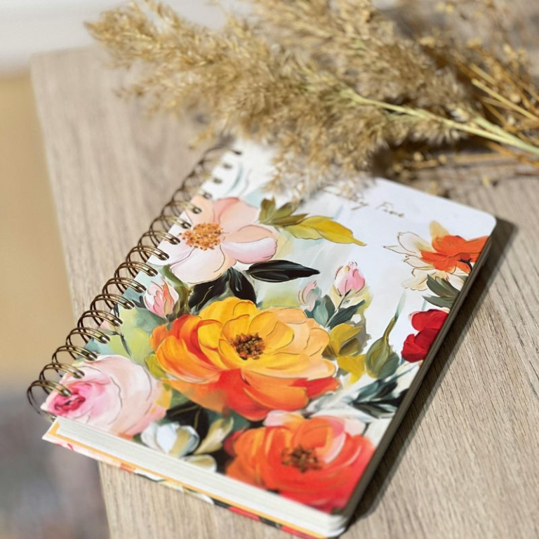 A floral cover journal sitting beside greenery on a wooden table