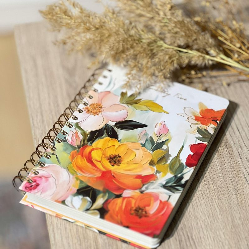 A floral cover journal sitting beside greenery on a wooden table